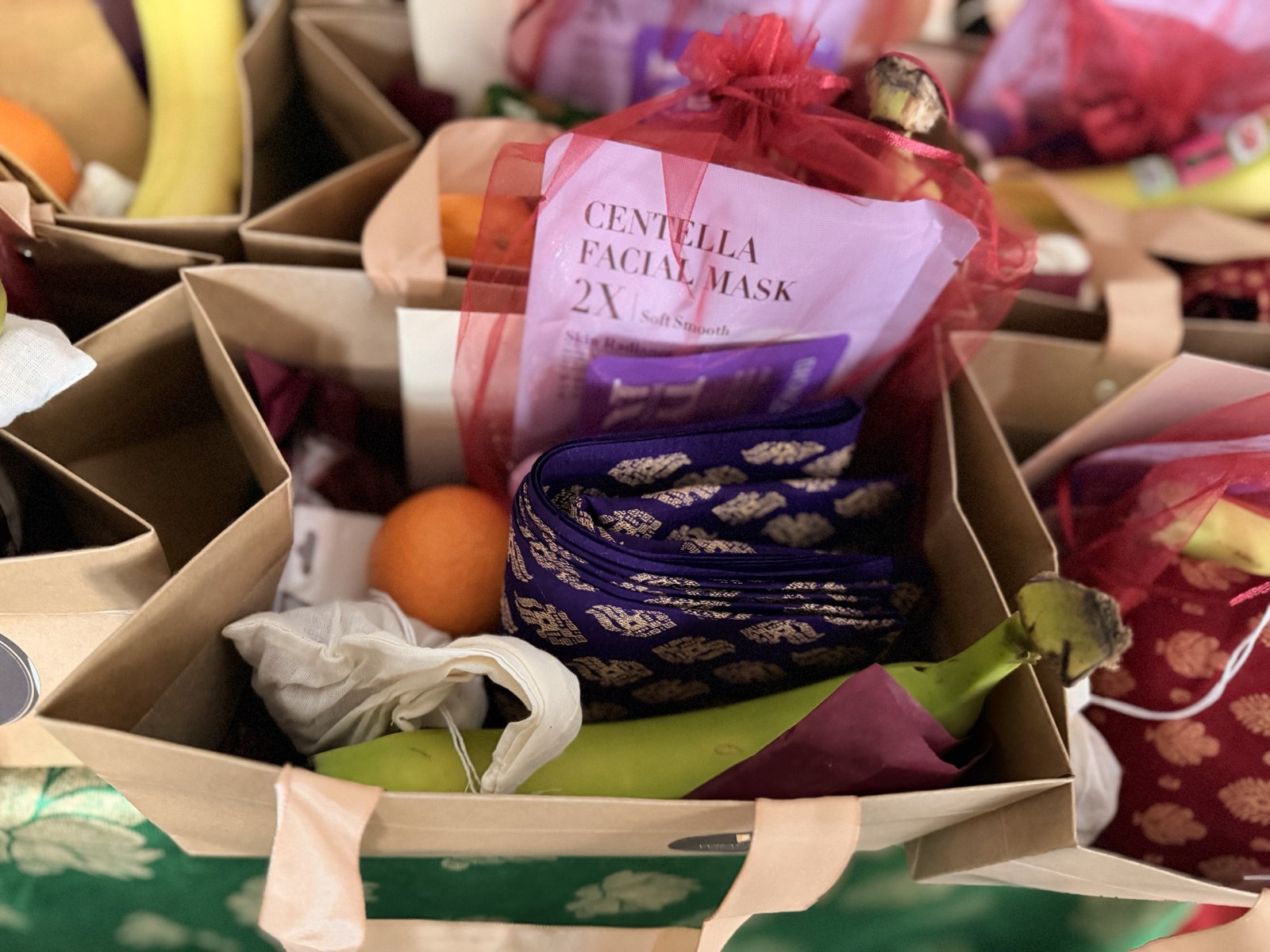 Inside one thamboolam bag: purple and gold silk blouse piece, cotton potli, banana, orange, and a red organza pouch with a keepsake