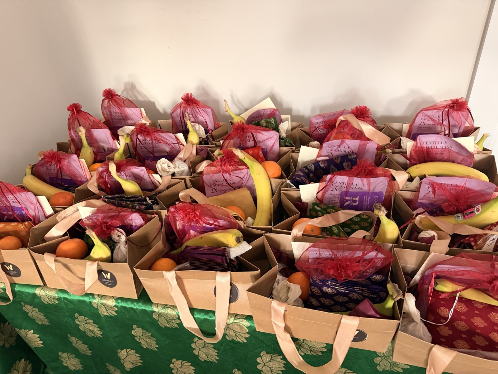 Twenty-five Wraptura thamboolam bags lined up on a green silk cloth ready for a Varalakshmi gathering